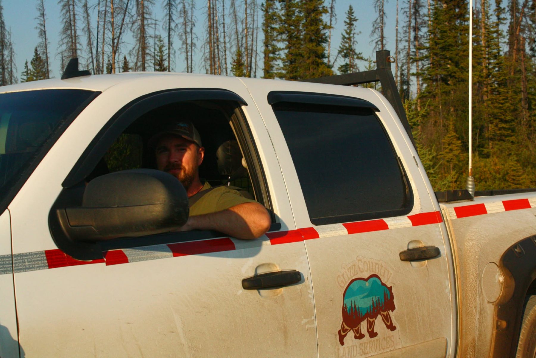 Daniel Cupples at the wheel of the Grizz Country truck, logo on the door, spruce behind